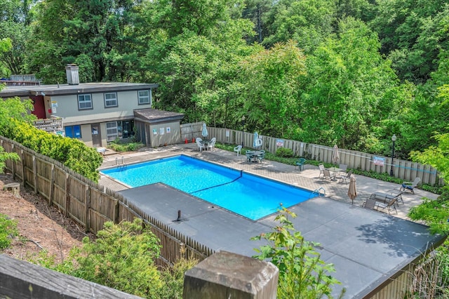 community pool featuring a patio area, a fenced backyard, and a forest view
