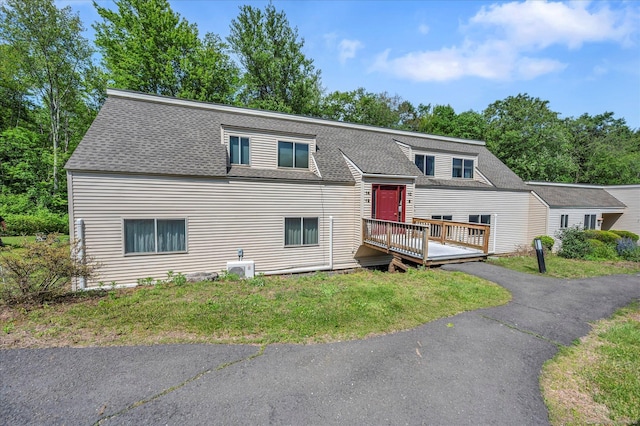 view of front of property featuring a wooden deck, a shingled roof, and a front lawn