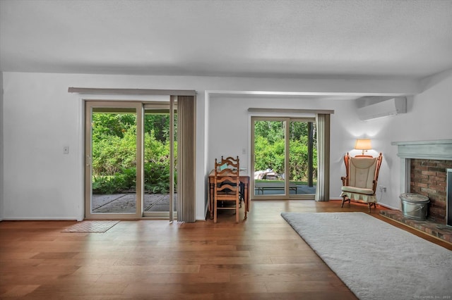 living area with a wall unit AC, wood finished floors, a brick fireplace, and baseboards