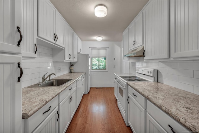 kitchen with white appliances, under cabinet range hood, a sink, light countertops, and backsplash