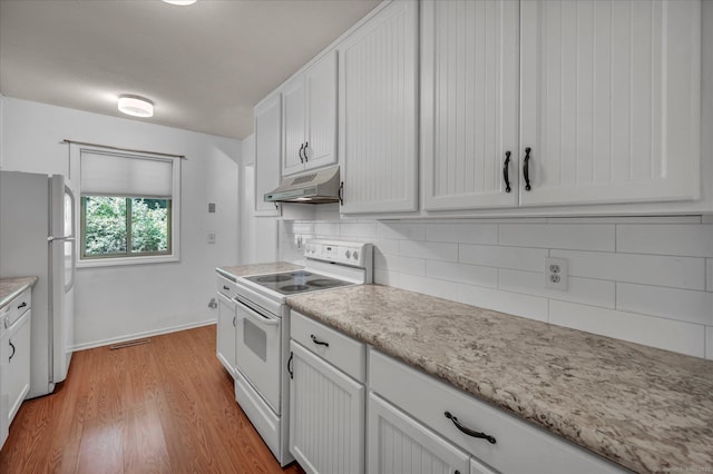kitchen featuring white appliances, under cabinet range hood, backsplash, and light wood-style floors