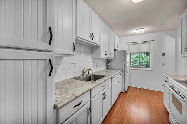 kitchen featuring a sink, decorative backsplash, light countertops, white appliances, and light wood finished floors
