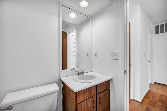 half bathroom featuring toilet, vanity, wood finished floors, and baseboards