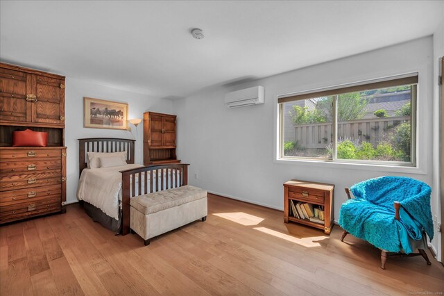 bedroom featuring a wall mounted air conditioner, light wood-style floors, and baseboards