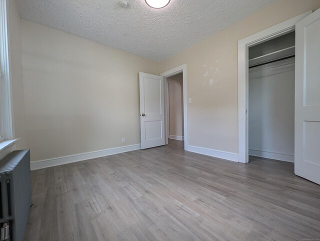 26 Westfield St, Manchester, CT 06042 - unfurnished bedroom with radiator, light wood finished floors, a textured ceiling, baseboards, and a closet