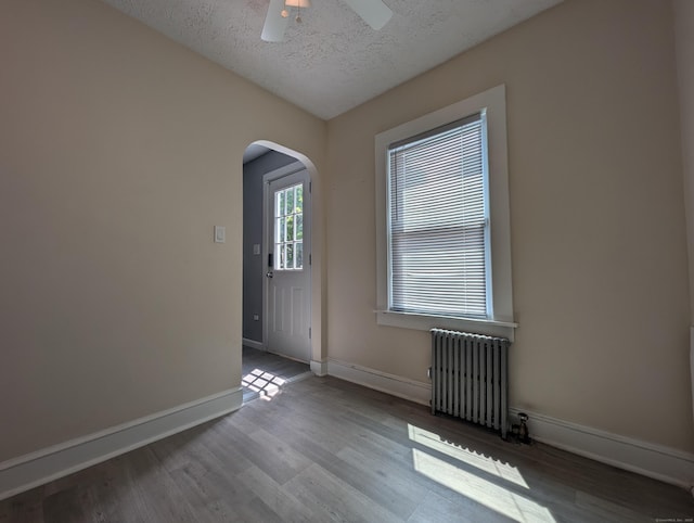 26 Westfield St, Manchester, CT 06042 - empty room with radiator heating unit, arched walkways, wood finished floors, baseboards, and a textured ceiling