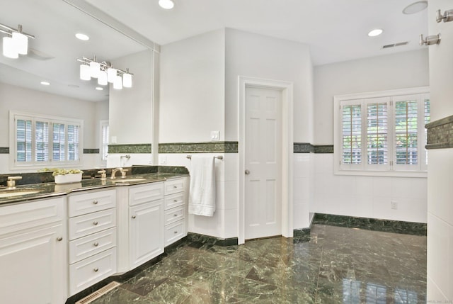 19 Father Peters Ln, New Canaan, CT 06840 - bathroom with double vanity, plenty of natural light, a wainscoted wall, marble tiled flooring, and tile walls