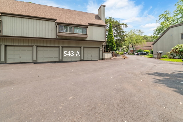 543 Heritage Vlg Unit A, Southbury, CT 06488 - view of property exterior featuring a chimney, a shingled roof, a garage, and driveway