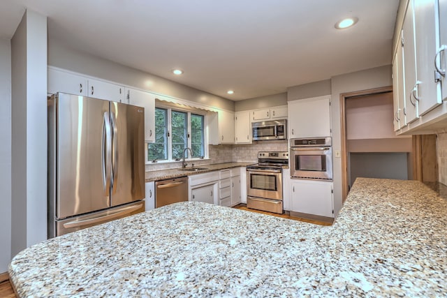 15 Edgemere Rd, Hamden, CT 06517 - kitchen with appliances with stainless steel finishes, a peninsula, backsplash, white cabinetry, and light stone countertops