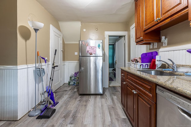3800 Main St, Stratford, CT 06614 - kitchen featuring appliances with stainless steel finishes, a sink, a wainscoted wall, light wood finished floors, and light stone counters