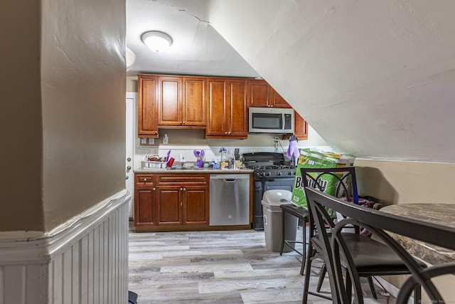 3800 Main St, Stratford, CT 06614 - kitchen featuring appliances with stainless steel finishes, light wood-style floors, brown cabinets, and a wainscoted wall