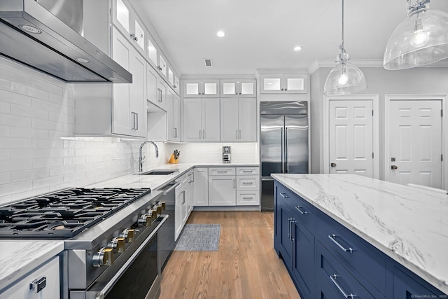 868 S Pine Creek Rd, Fairfield, CT 06824 - kitchen featuring appliances with stainless steel finishes, wall chimney range hood, white cabinets, a sink, and light wood-style flooring