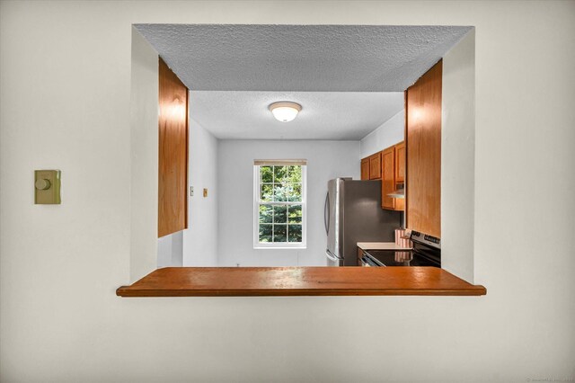 745 Merrow Rd Apt 157, Coventry, CT 06238 - kitchen with stainless steel appliances, a textured ceiling, brown cabinets, and exhaust hood