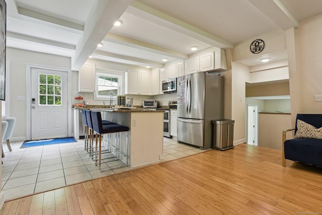 958 Essex Rd, Westbrook, CT 06498 - kitchen with stainless steel appliances, beamed ceiling, light wood finished floors, a kitchen bar, and white cabinets