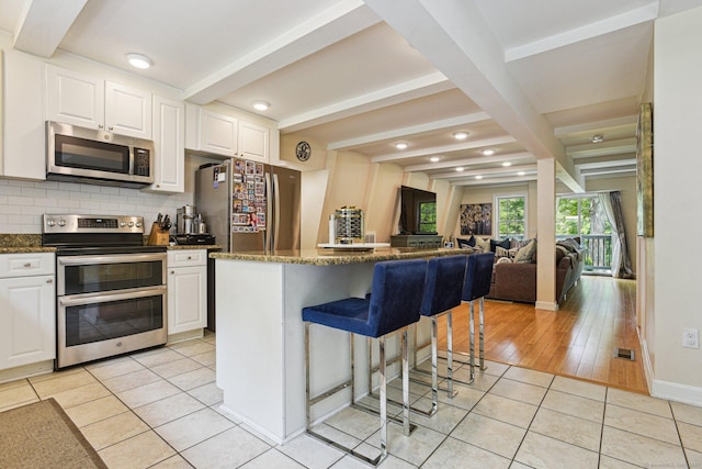 958 Essex Rd, Westbrook, CT 06498 - kitchen featuring stainless steel appliances, beamed ceiling, light tile patterned floors, a kitchen breakfast bar, and backsplash