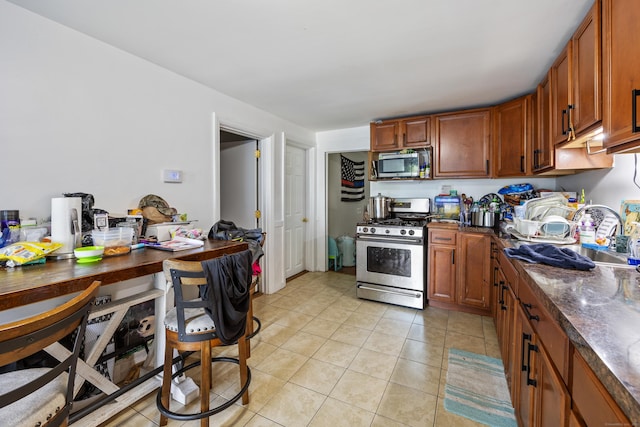 60 Albert St, Torrington, CT 06790 - kitchen with appliances with stainless steel finishes, dark countertops, light tile patterned flooring, brown cabinets, and a sink