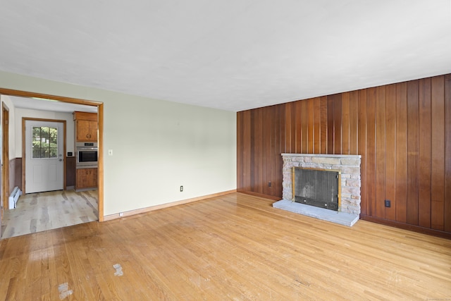 26 Caroldon Rd, Middletown, CT 06457 - unfurnished living room featuring light wood-style flooring, a fireplace, wooden walls, and a baseboard radiator