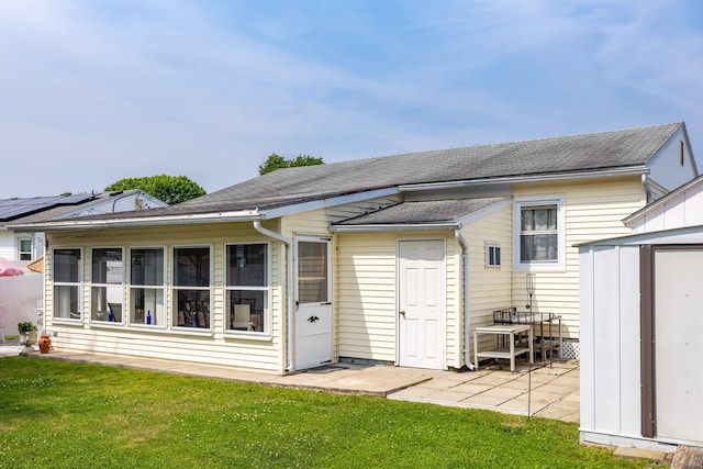 rear view of property featuring a shed, a sunroom, a patio area, a lawn, and a shingled roof