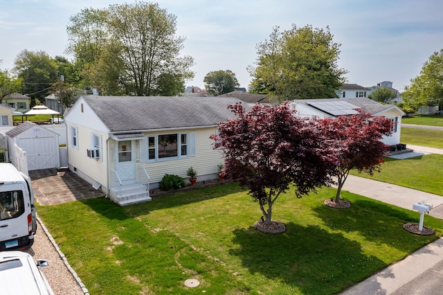 view of front facade with a shingled roof, a front yard, entry steps, and a shed