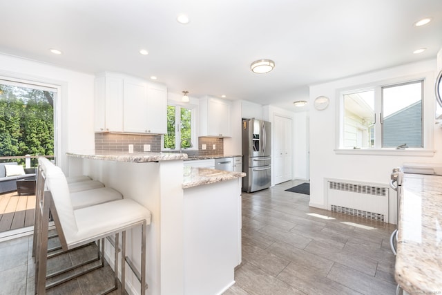 100 Grandview St, Manchester, CT 06040 - kitchen featuring appliances with stainless steel finishes, radiator, tasteful backsplash, white cabinetry, and light stone counters