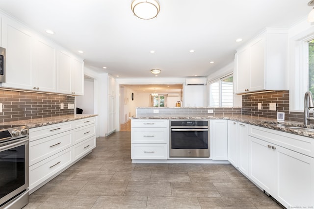 100 Grandview St, Manchester, CT 06040 - kitchen with appliances with stainless steel finishes, a sink, an AC wall unit, decorative backsplash, and a peninsula