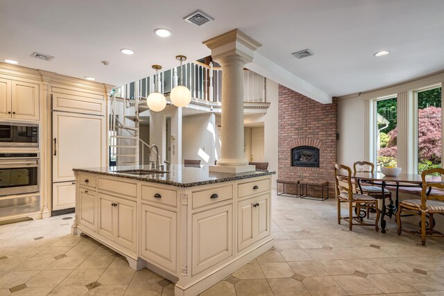 15 NE Rd, Farmington, CT 06032 - kitchen featuring cream cabinets, stainless steel appliances, decorative columns, a brick fireplace, and light tile patterned flooring