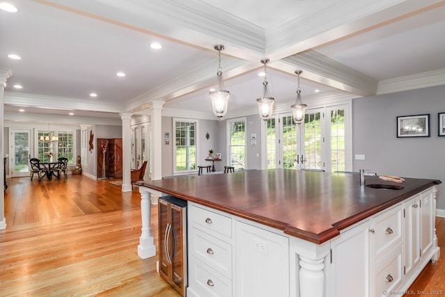 kitchen featuring beverage cooler, ornate columns, light wood-style floors, plenty of natural light, and ornamental molding