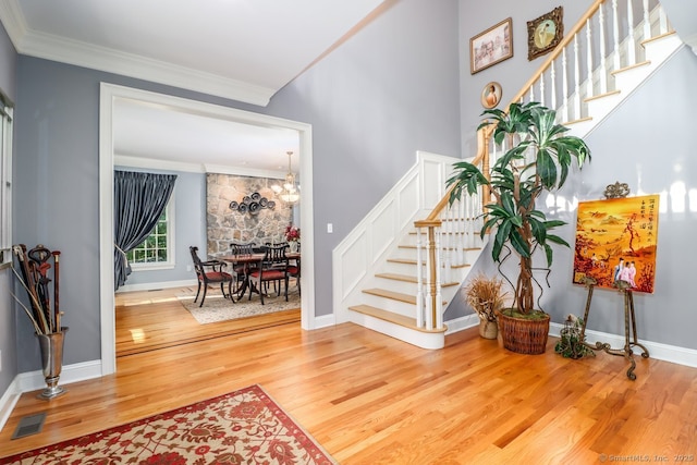 foyer featuring wood finished floors, crown molding, stairs, a chandelier, and baseboards