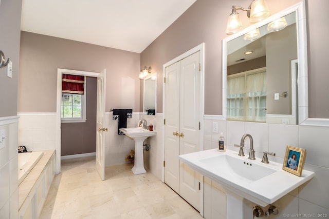 bathroom featuring a sink, tiled bath, tile walls, and a wainscoted wall