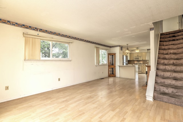 269 Captain Thomas Blvd Unit 12, West Haven, CT 06516 - unfurnished living room featuring stairway, light wood finished floors, plenty of natural light, a textured ceiling, and baseboards