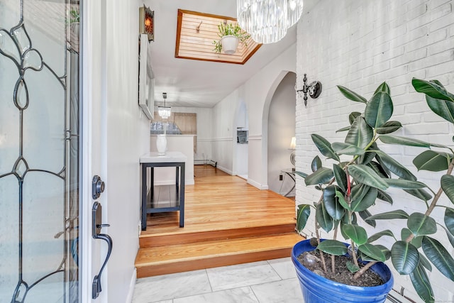 575 W Todd St, Hamden, CT 06518 - entrance foyer featuring arched walkways, light marble finish floors, a chandelier, brick wall, and a baseboard heating unit