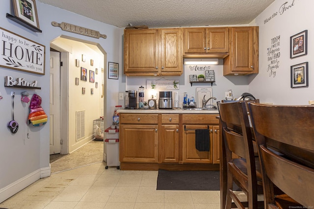 72 Beech St, Bristol, CT 06010 - kitchen featuring arched walkways, brown cabinetry, a textured ceiling, and light countertops