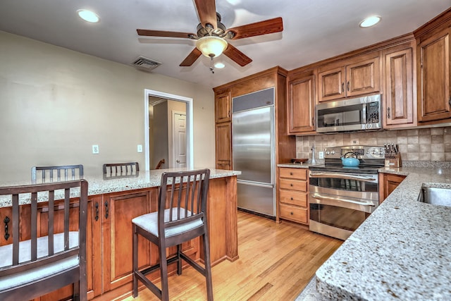 17 Farmstead Ln, West Hartford, CT 06117 - kitchen with appliances with stainless steel finishes, light wood finished floors, a ceiling fan, brown cabinetry, and light stone countertops