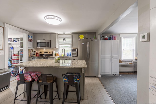 12 John St, Killingly, CT 06239 - kitchen featuring appliances with stainless steel finishes, a breakfast bar, a kitchen island, gray cabinetry, and light wood-style flooring