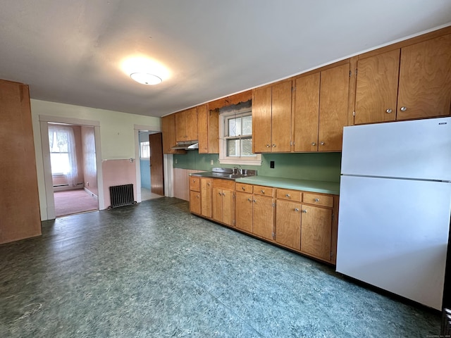 189 N Main St, Griswold, CT 06351 - kitchen featuring freestanding refrigerator, radiator heating unit, under cabinet range hood, and brown cabinetry