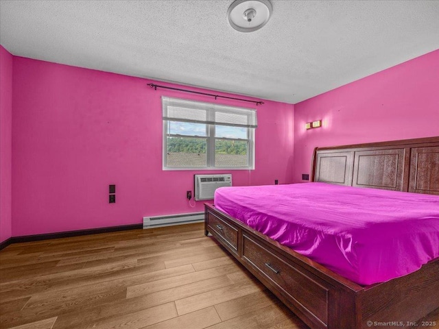 1081 New Haven Rd Apt 12F, Naugatuck, CT 06770 - bedroom with baseboard heating, a wall mounted air conditioner, wood finished floors, a textured ceiling, and baseboards