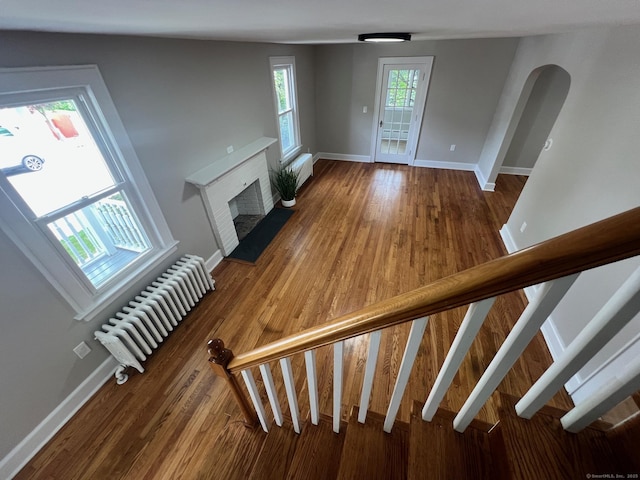28 Highland Ave, Naugatuck, CT 06770 - unfurnished living room featuring radiator heating unit, a fireplace, wood finished floors, arched walkways, and stairs