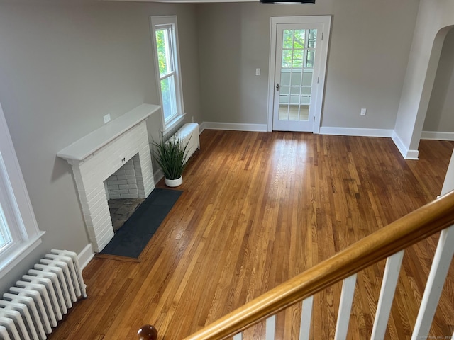 28 Highland Ave, Naugatuck, CT 06770 - unfurnished living room with radiator heating unit, a brick fireplace, wood finished floors, and arched walkways