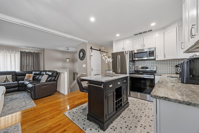 7 Pleasant St, Wolcott, CT 06716 - kitchen featuring appliances with stainless steel finishes, white cabinets, a barn door, light stone countertops, and dark cabinetry