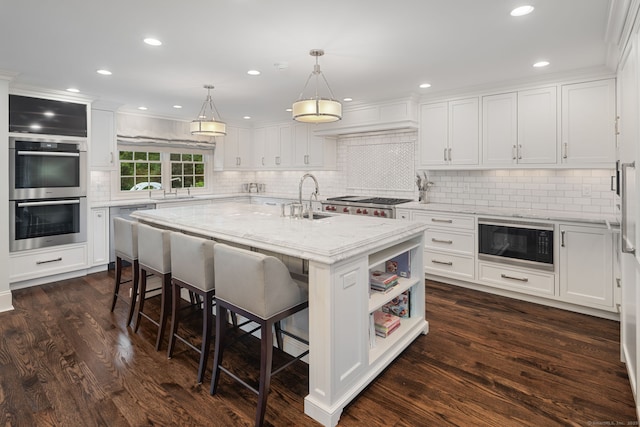 133 Buttery Rd, New Canaan, CT 06840 - kitchen with black microwave, double oven, white cabinets, a breakfast bar, and a center island with sink