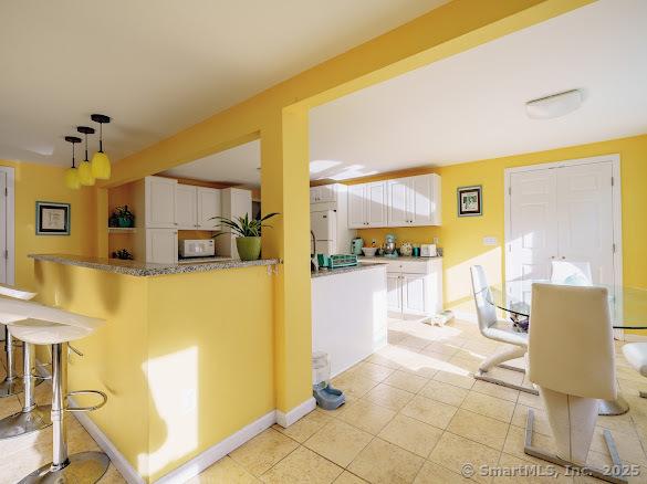 847 Glenbrook Rd, Orange, CT 06477 - kitchen with white cabinets, a kitchen bar, light tile patterned flooring, hanging light fixtures, and white microwave