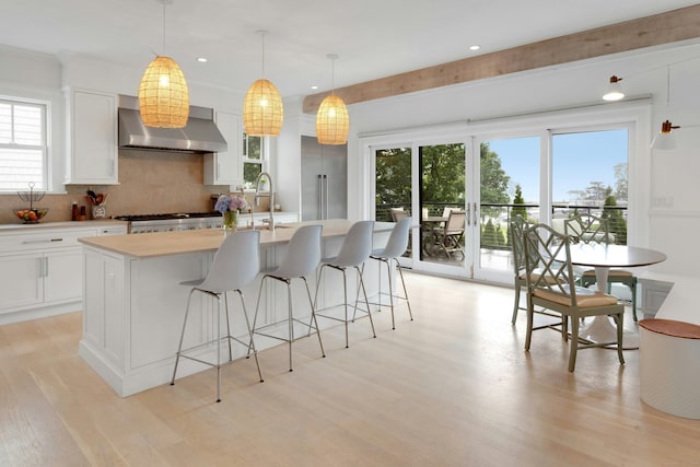 47 Pine Point Rd, Norwalk, CT 06853 - kitchen with wall chimney exhaust hood, light countertops, tasteful backsplash, light wood finished floors, and a kitchen island with sink