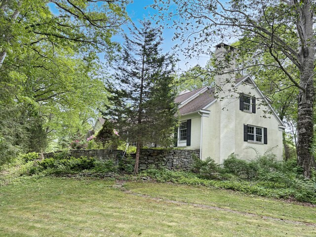 206 Peddlers Rd, Guilford, CT 06437 - view of home's exterior featuring stucco siding, a chimney, a lawn, and roof with shingles
