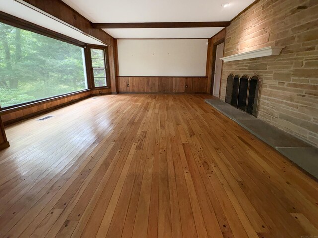 206 Peddlers Rd, Guilford, CT 06437 - unfurnished living room featuring hardwood / wood-style floors, beam ceiling, wooden walls, a stone fireplace, and wainscoting