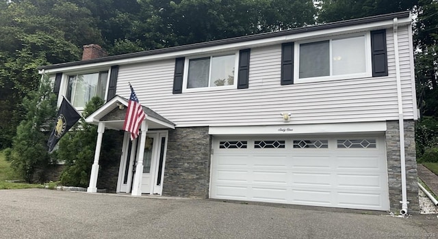 view of front of house with driveway, a chimney, an attached garage, and stone siding