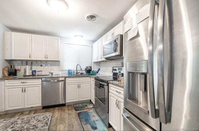 kitchen with appliances with stainless steel finishes, wood finished floors, tasteful backsplash, and white cabinetry