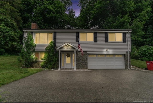 view of front of home with asphalt driveway, a garage, a chimney, a yard, and stone siding
