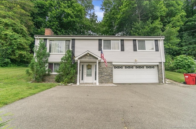 view of front facade featuring driveway, an attached garage, a chimney, stone siding, and a front lawn