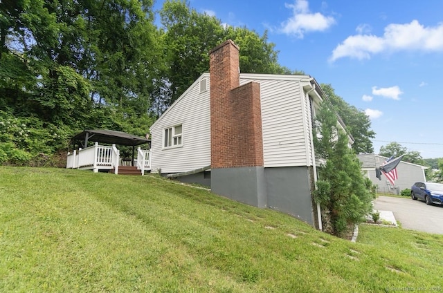 view of home's exterior featuring a chimney, a yard, a wooden deck, and concrete driveway