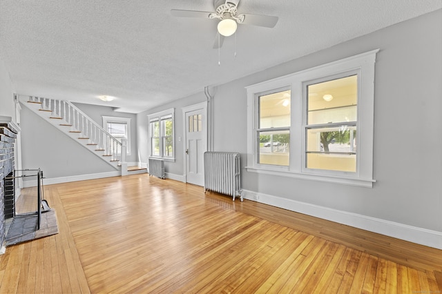 471 New Britain Rd, Berlin, CT 06037 - unfurnished living room featuring radiator heating unit, a textured ceiling, stairway, light wood-type flooring, and a brick fireplace